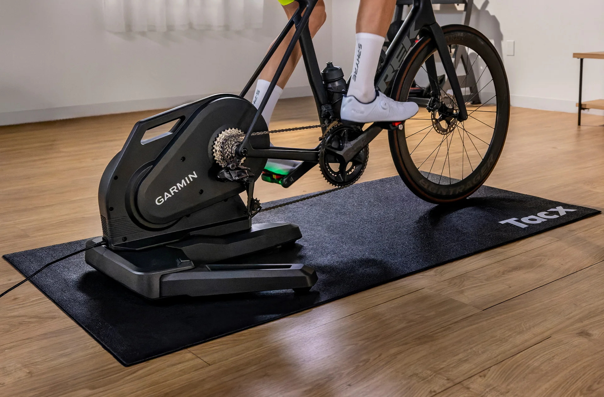 Trenażer rowerowy Tacx Nēra umieszczony na czarnej macie podłogowej Tacx