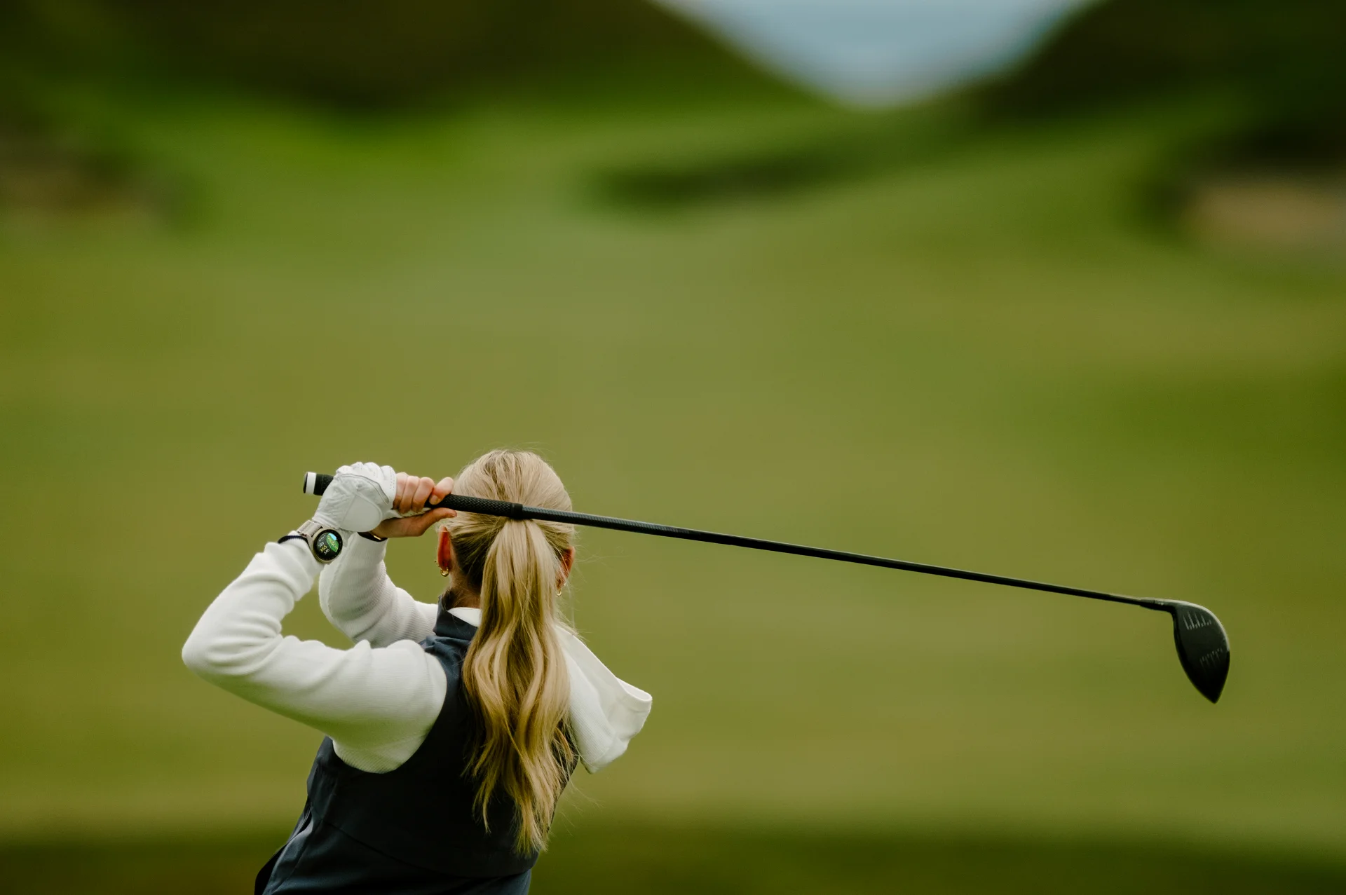 Kobieta wykonująca uderzenie kijem golfowym i patrząca w dal