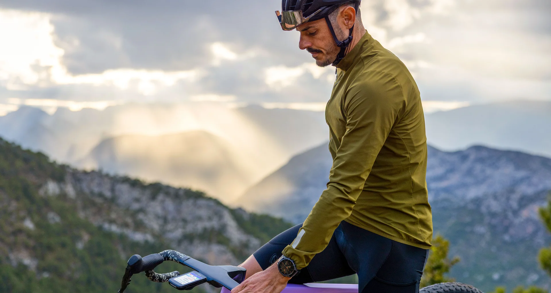 Kolarz spoglądający na licznik Garmin Edge 1060 zamontowany na rowerze, w oddali widać góry